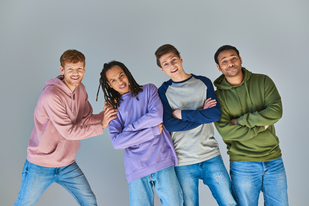 four cheerful men in casual outfits smiling at camera posing on grey backdrop, cultural diversity